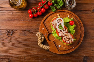 Lezzetli ton balıklı sandviç, marul, domates ve soğanlı. Arka planda doğal ahşap. Üst görünüm.