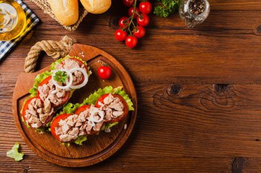 Lezzetli ton balıklı sandviç, marul, domates ve soğanlı. Arka planda doğal ahşap. Üst görünüm.