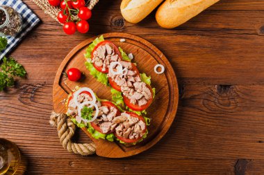 Lezzetli ton balıklı sandviç, marul, domates ve soğanlı. Arka planda doğal ahşap. Üst görünüm.