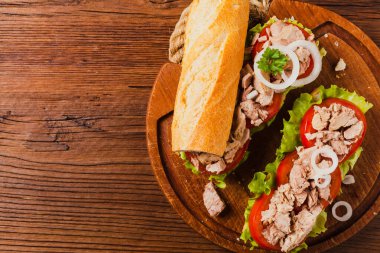 Lezzetli ton balıklı sandviç, marul, domates ve soğanlı. Arka planda doğal ahşap. Üst görünüm.