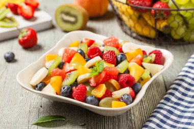Taze meyveli lezzetli meyve salatası. Arkadaki tahta, gri masa. Ön görünüm.