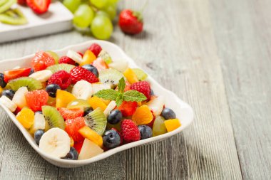 Taze meyveli lezzetli meyve salatası. Arkadaki tahta, gri masa. Ön görünüm.
