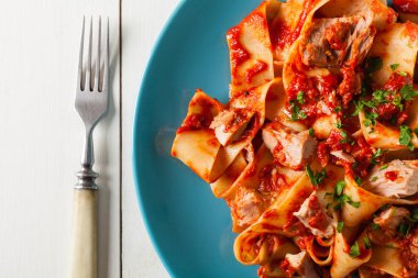 Domates soslu, ton balıklı pappardelle makarna. Mavi tabakta servis edilmiş, arka planda beyaz panolar. Üst görünüm. 