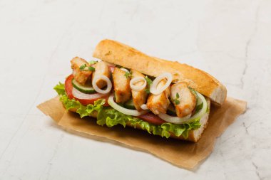 Domatesli tavuklu sandviç, salatalık, marul ve soğanlı. Beyaz taş arka plan. Ön görünüm. 