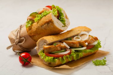 Domatesli tavuklu sandviç, salatalık, marul ve soğanlı. Beyaz taş arka plan. Ön görünüm. 