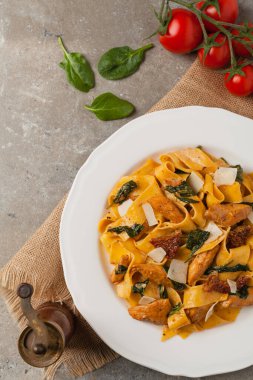 İtalyan salatası, pappardelle makarna, ıspanak, ızgara tavuk ve kurutulmuş domates, üzerine peynir serpiştirilmiş. Üst Manzara. Taş arkaplan.