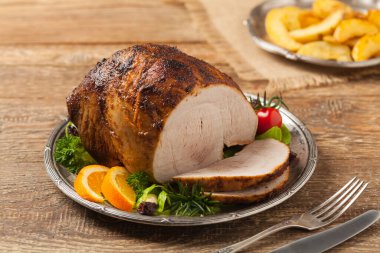 Fırında jambon, eski bir tabakta servis edilir. Doğal ahşap arka plan. Ön görünüm.