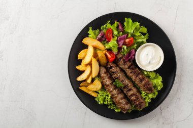 Geleneksel cevapcici fırında patates ile servis edilir. Düz yatıyordu. Taş zemin. Üst görünüm.