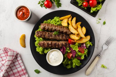 Geleneksel cevapcici fırında patates ile servis edilir. Düz yatıyordu. Taş zemin. Üst görünüm.