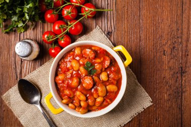 Domates soslu fırınlanmış fasulye, sarı kaselerde servis edilir. Üst görünüm. 