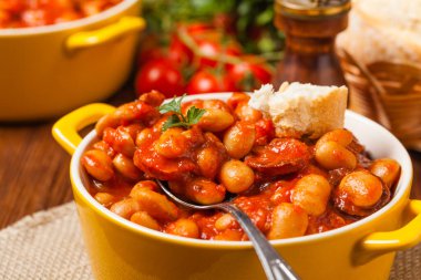 Domates soslu fırınlanmış fasulye, sarı kaselerde servis edilir. Ön görünüm. 