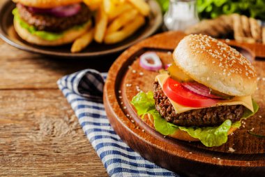 Ev yapımı, peynirli ve sebzeli sığır burger. Patates kızartmasıyla servis edilmiş. Ön görünüm.