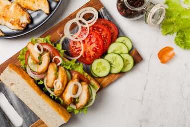 Domatesli tavuklu sandviç, salatalık, marul ve soğanlı. Beyaz taş arka plan. Üst Manzara. Düz yatıyordu.