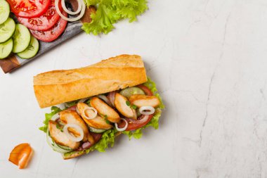 Domatesli tavuklu sandviç, salatalık, marul ve soğanlı. Beyaz taş arka plan. Üst Manzara. Düz yatıyordu.