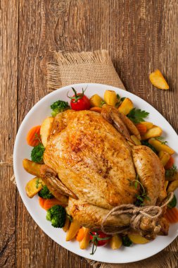Kızarmış tavuk bütünü. Sebze ve fırında patatesle servis edilmiş. Düz yatıyordu. Üst görünüm. 