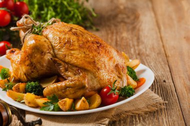 Kızarmış tavuk bütünü. Sebze ve fırında patatesle servis edilmiş. Ön görünüm. 