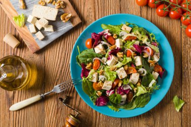 Tofulu, domatesli ve cevizli nefis salata, üzerine balzamik sirke serpilmiş ve mavi bir tabakta servis edilmiş. Üst görünüm.