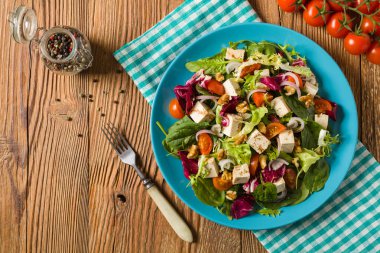 Tofulu, domatesli ve cevizli nefis salata, üzerine balzamik sirke serpilmiş ve mavi bir tabakta servis edilmiş. Üst görünüm.