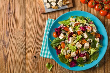 Tofulu, domatesli ve cevizli nefis salata, üzerine balzamik sirke serpilmiş ve mavi bir tabakta servis edilmiş. Üst görünüm.