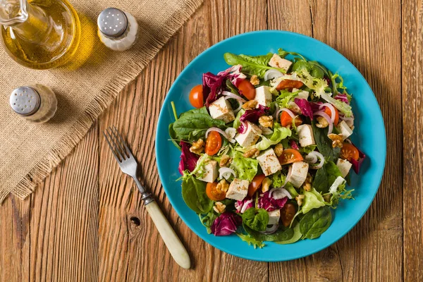 Tofulu, domatesli ve cevizli nefis salata, üzerine balzamik sirke serpilmiş ve mavi bir tabakta servis edilmiş. Üst görünüm.