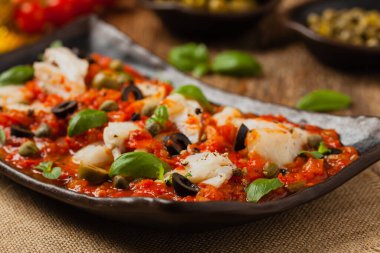 İtalyan usulü morina, domatesli zeytin ve kapari. Ön görünüm.