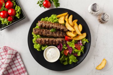 Geleneksel cevapcici fırında patates ile servis edilir. Düz yatıyordu. Taş zemin. Üst görünüm.