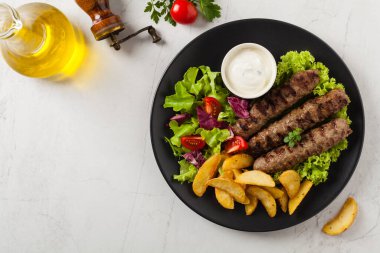 Geleneksel cevapcici fırında patates ile servis edilir. Düz yatıyordu. Taş zemin. Üst görünüm.
