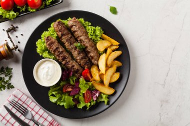 Geleneksel cevapcici fırında patates ile servis edilir. Düz yatıyordu. Taş zemin. Üst görünüm.