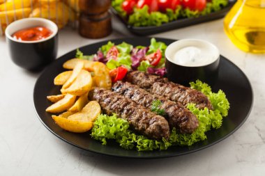 Geleneksel cevapcici fırında patates ile servis edilir. Taş zemin. Ön görünüm.