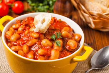 Domates soslu fırınlanmış fasulye, sarı kaselerde servis edilir. Ön görünüm. 