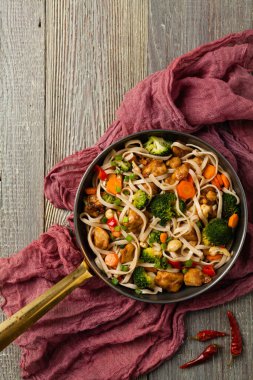 Tavuk, brokoli ve havuçla karıştırılmış makarna. Üst Manzara. Gri ahşap arka plan. Kızartma tavasında servis edilir..