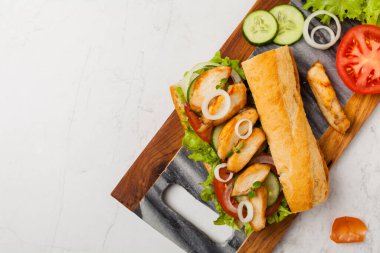 Domatesli tavuklu sandviç, salatalık, marul ve soğanlı. Beyaz taş arka plan. Üst Manzara. Düz yatıyordu.