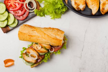 Domatesli tavuklu sandviç, salatalık, marul ve soğanlı. Beyaz taş arka plan. Üst Manzara. Düz yatıyordu.