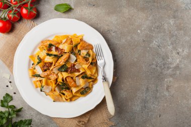 İtalyan salatası, pappardelle makarna, ıspanak, ızgara tavuk ve kurutulmuş domates, üzerine peynir serpiştirilmiş. Üst Manzara. Taş arkaplan.