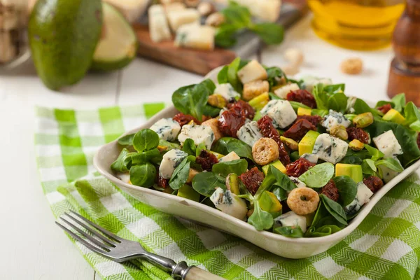 Italian salad with avocado, gorgonzola cheese, pistachio nuts, sun-dried tomatoes and croutons. Front view. White woodem background.