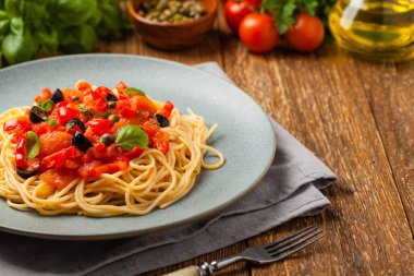 Domates ve zeytinli İtalyan spagetti alla Pultanesca. Et ve peynir olmadan servis edilir. Ön manzara. Doğal ahşap zemin. 