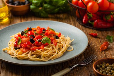Domates ve zeytinli İtalyan spagetti alla Pultanesca. Et ve peynir olmadan servis edilir. Ön manzara. Doğal ahşap zemin. 