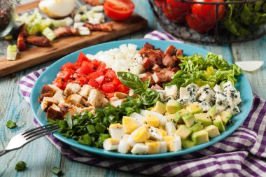 Cobb salad.  Main-dish American garden salad typically made with chopped salad greens , tomato, crisp bacon, boiled, grilled chicken breast, hard-boiled eggs, avocado, chives, Roquefort cheese, and red-wine vinaigrette. Front view.  clipart