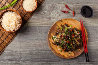 Geleneksel Kore Bulgogi yemeği. İnce dilimlenmiş, ızgara sığır eti, pirinç ve sebzelerle servis edilmiş. Üst Manzara. Doğal ahşap zemin.