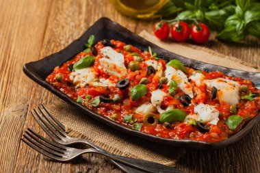 İtalyan usulü morina, domatesli zeytin ve kapari. Ön görünüm.