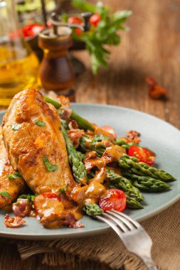 Kızarmış tavuk göğsü, kuşkonmazla servis edilen domates sosu, kurutulmuş domates. Ön görünüm.