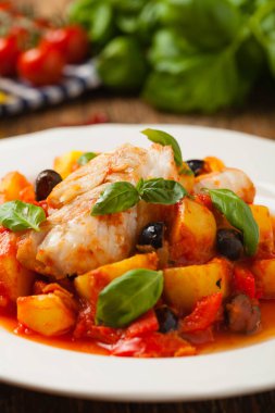 Geleneksel ispanyolca morina balığı. Domates sosunda haşlanmış patates, olivki ve fesleğen ile servis edilmiş. Ön görünüm. 