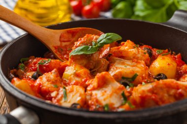 Geleneksel ispanyolca morina balığı. Domates sosunda haşlanmış patates, olivki ve fesleğen ile servis edilmiş. Ön görünüm. 