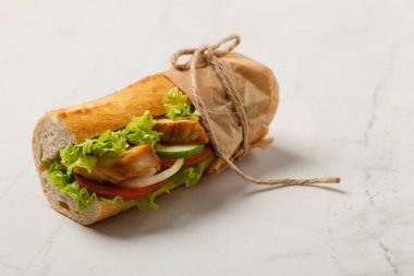 Domatesli tavuklu sandviç, salatalık, marul ve soğanlı. Beyaz taş arka plan. Ön görünüm. 