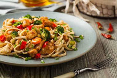 Tavuk, brokoli ve havuçla karıştırılmış makarna. Gri bir tabakta servis edilir..