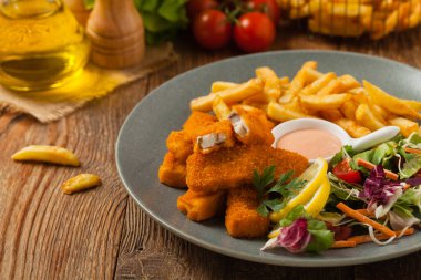 Patates kızartmalı balık ve gri tabakta salata. Ön görünüm.