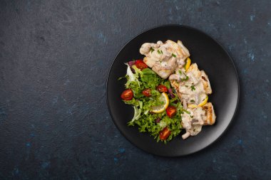 Mantar soslu kızarmış morina balığı ve salata. Siyah bir tabakta porsiyon. Koyu arkaplan.