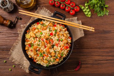 Tavuklu pilav. Bir tavada hazırlandı ve servis edildi. Arka planda doğal ahşap. Üst görünüm.