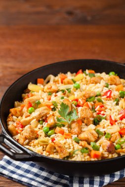 Tavuklu pilav. Bir tavada hazırlandı ve servis edildi. Arka planda doğal ahşap. Ön görünüm.