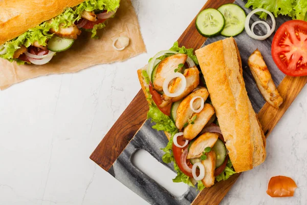 Chicken sandwich with tomato, cucumber, lettuce and onions. White stone background. Top view. Flat lay.